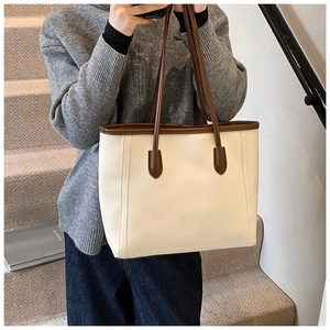 Close-up of a large beige tote bag with brown handles on a minimalist staircase