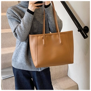 Brown leather tote bag worn by model on stairs showing its large capacity and drape