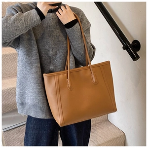 Close-up of caramel leather tote bag with leaf-shaped strap reinforcement and smooth finish