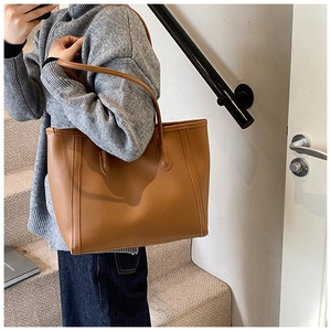 Brown leather tote bag held by a model on stairs, showing the large commuter style capacity