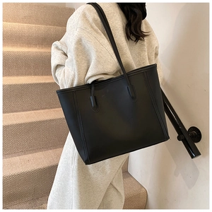 Minimalist black tote bag with long handles shown on model in a modern interior setting