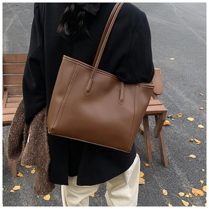 Rear view of a dark brown leather tote bag worn over the shoulder in an autumn street setting