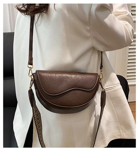Detail of dark brown leather saddle bag with wave flap and vintage woven strap on model