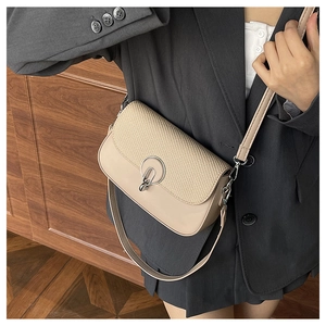 Detail of beige crossbody bag with textured woven flap and round metal clasp on a model