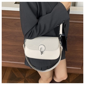 Detail of ivory faux leather crossbody bag with textured panel and silver circular buckle