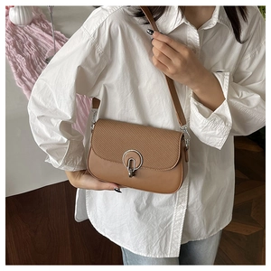 Close-up of brown crossbody bag featuring woven texture flap and silver metal lock