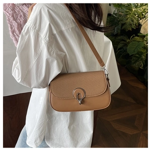 Detail of caramel brown shoulder bag with woven texture and round silver metal buckle