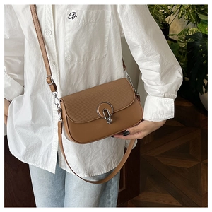 Detail of a brown crossbody bag with textured patchwork flap and silver round lock