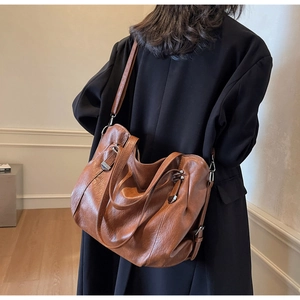Detailed view of the brown leather tote bag texture and silver hardware on a shoulder strap