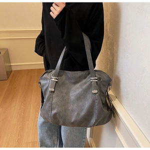 Deep grey tote bag with textured leather surface and silver metal buckle worn by model