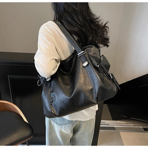 Close-up of black leather tote bag featuring adjustable strap and silver metal hardware