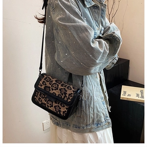 Detail of leopard print crossbody bag with black trim worn by a model in casual style