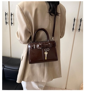 Détail du sac à main en cuir verni marron foncé avec boucle et breloque métallique