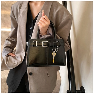 Gros plan d'un sac à main en cuir verni noir avec boucle argentée et breloque clé dorée
