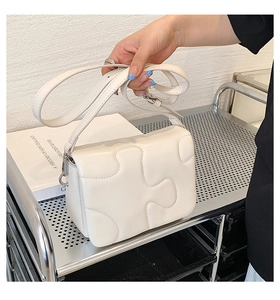 Detail shot of cream white crossbody bag with jigsaw puzzle embossed texture and silver hardware