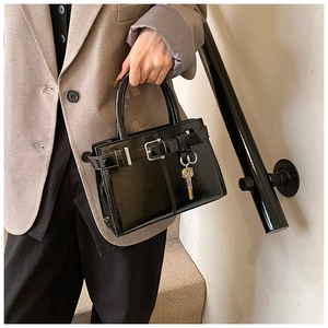 Gros plan détaillé du sac à main noir brillant avec boucle argentée et breloque en métal