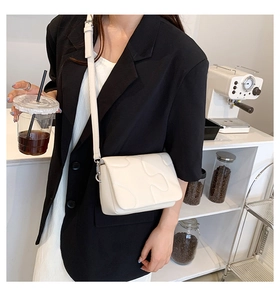 Detailed view of cream-white quilted crossbody bag with wave stitching and slim strap