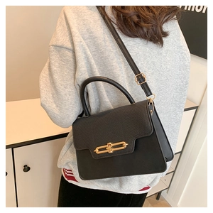 Close-up of elegant black crossbody bag featuring textured flap and gold metal bar lock