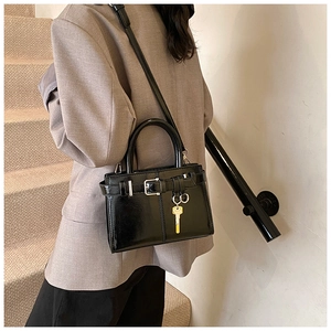 Détail du sac à main noir en cuir verni avec boucle et pendentif clé dorée