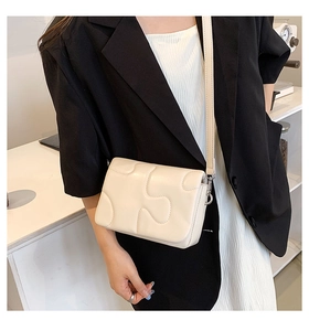 Close-up of cream crossbody bag featuring puzzle stitch pattern and silver buckle detail