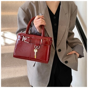 Détail du sac à main bordeaux avec boucle de ceinture et breloque clé tenu par mannequin