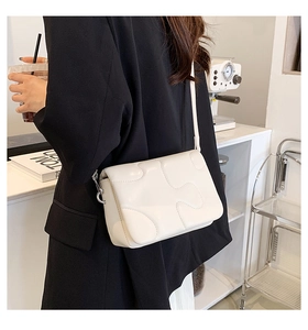 Close-up of white crossbody bag with puzzle stitch texture and silver metal hardware