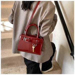 Détail du sac à main bordeaux en cuir verni avec boucle décorative et breloque clé