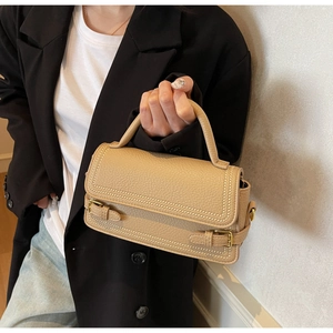 Close-up of beige lychee textured leather handbag with white double stitching details