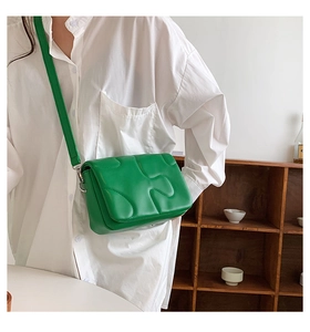 Side view of a trendy quilted green crossbody square bag on a model in a warm setting