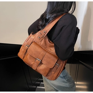 Detail of tan leather shoulder bag with buckle pockets shown on model against stairs
