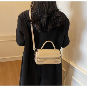 Detail of light apricot lychee pattern leather bag with white stitching and gold buckle