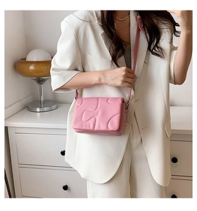 Pink quilted crossbody bag with puzzle texture and adjustable strap on a model