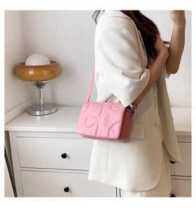 Pink puzzle-style embossed quilted shoulder bag shown on a white blazer outfit