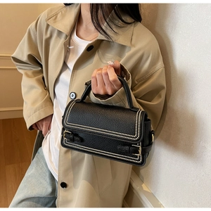 Close-up of black lychee grain leather crossbody bag with golden rivet trim and metal buckles