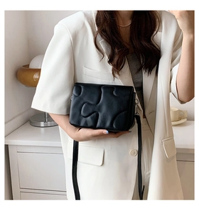 Detail of black crossbody bag with puzzle stitching pattern worn over white suit