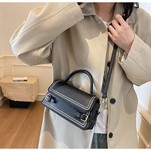 Detail of black lychee texture crossbody bag with white dot trim and metal buckle straps