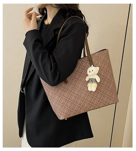 Detail view of large brown printed tote bag with thin straps and cute plush bear charm