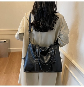 Détails d'un grand sac cabas noir porté par un mannequin avec texture en cuir brillant