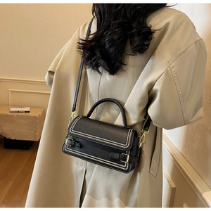 Detail of black lychee grain leather bag with white stitching and gold buckles