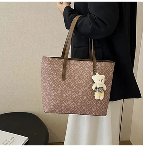 Detail of tan tote bag with letter print and a cute plush bear charm on handle