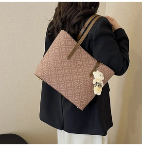 Close-up of brown vintage tote bag with letter print and cute plush bear charm accessory