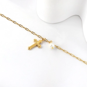 Gold paperclip anklet with cross pendant and pearl detail on white background