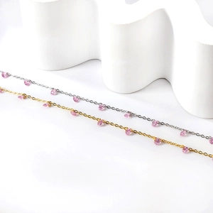 Détail de bracelets de cheville or et argent avec cristaux roses sur support vague
