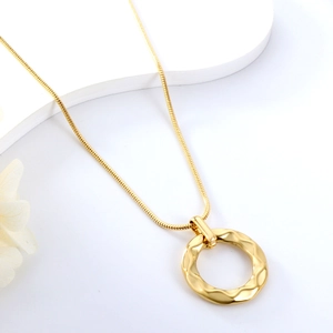 Détail d'un collier chaîne serpent dorée avec un pendentif texturé à motifs de vagues