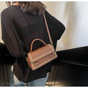 Detailed view of caramel brown lychee leather handbag with golden buckles and stitching