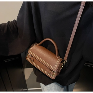 Brown litchi grain leather crossbody bag with rivet details shown on model