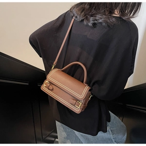 Brown lychee leather crossbody bag with gold stud details shown on model shoulder