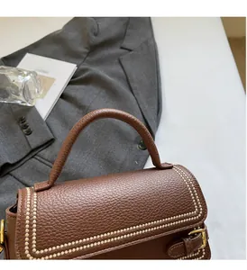 Detail of a brown leather handbag with pebble texture and gold stud accents on a suit