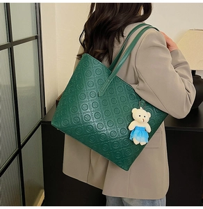Detail view of dark green tote bag featuring luxury embossed logo and cute bear pendant