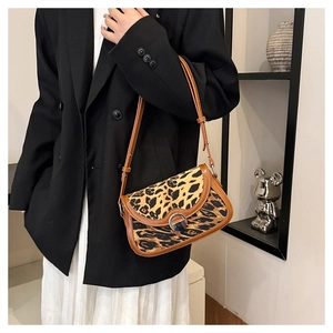 Close-up of leopard print saddle bag with adjustable brown strap and metal buckle